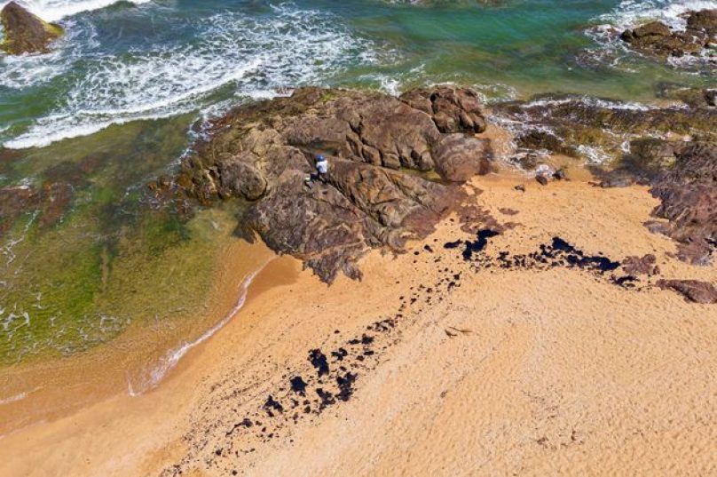 Voluntário tenta remover mancha de óleo da praia de Busca Vida, em Camaçari, na Bahia.