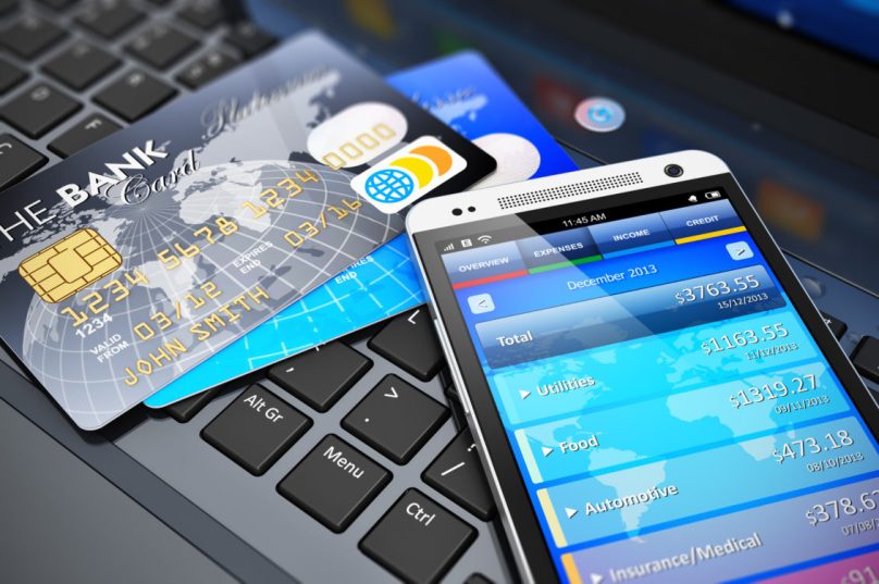 Mobile banking, financial success, accounting and electronic internet money payments business concept: macro view of stack of credit cards and modern touchscreen smartphone on office laptop keyboard with selective focus effect