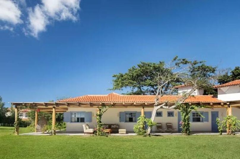 FACHADA | A reforma procurou manter a arquitetura original da casa, que é toda avarandada, com manutenção de janelas e portas e fachadas, pintadas de com a cor “Repouso Azul”, da Coral, que remete ao estilo arquitetônico típico de Búzios. Paisagismo assinado por André Piquet — Foto: MCA Estúdio/Divulgação
