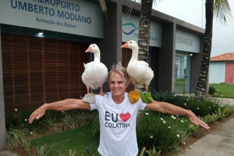 Sérgio Meneguelli em sua chegada no Aeroporto Umberto Modiano  posa com dois gansos trazidos por um admirador local/ Foto Prensa de Babel