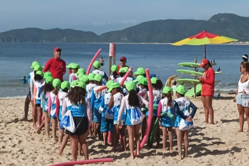 Crianças aprendem segurança no mar e preservação ambiental, enquanto pais participam de aulas funcionais / Divulgação