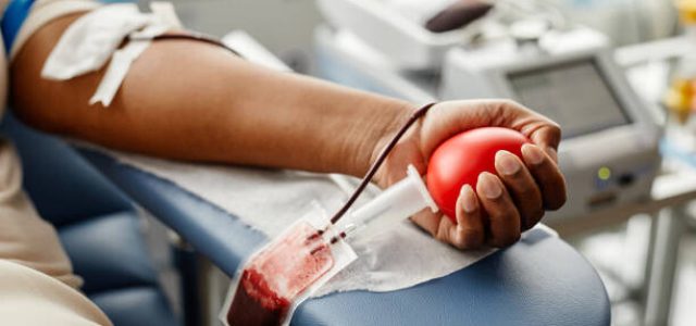 Closeup of black woman donating blood focus on hand holding red ball with tubing, copy space