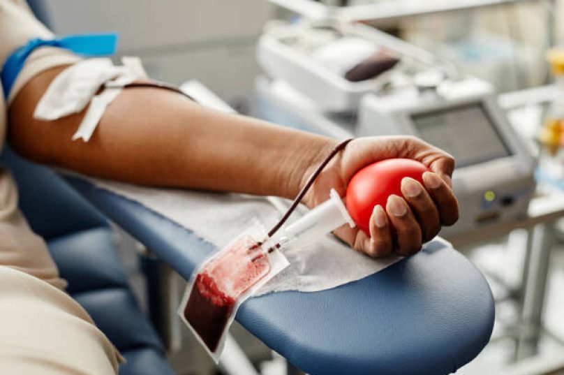 Closeup of black woman donating blood focus on hand holding red ball with tubing, copy space