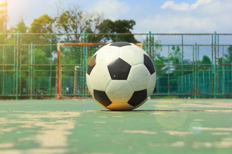 The ball on the middle of futball court and futsal goal as the background with sun flare
