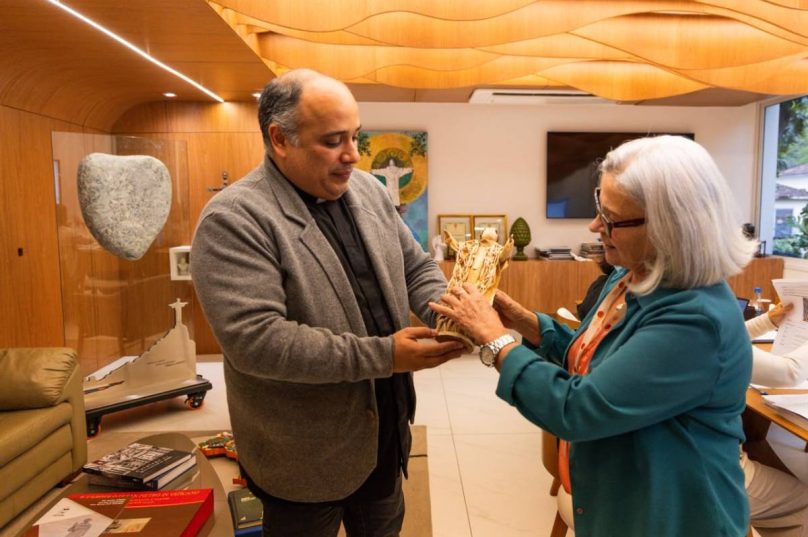 Eva Gomes entrega ao Padre Omar Raposo o retrato do sacerdote feito com fibras naturais. Ao lado da peça, a artesã e o reitor do Cristo Redentor registram o encontro que uniu arte, fé e afeto.