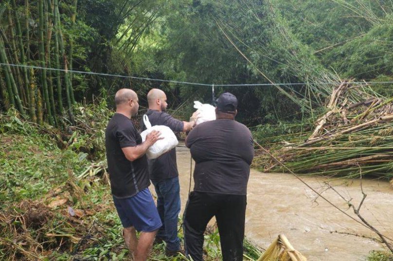 Moradores do Sana usam cordas para atravessar mantimentos e resgatar ilhados após a cheia dos rios; igrejas locais organizam doações enquanto equipes públicas atuam na região