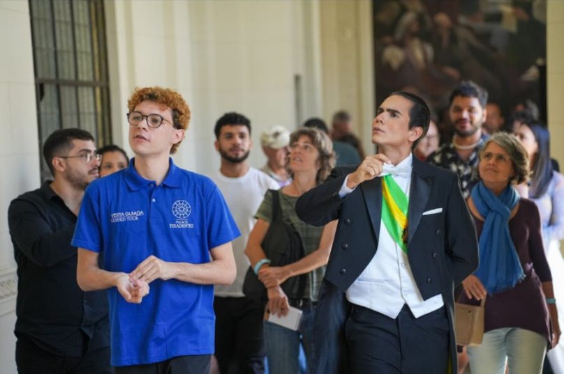 A Assembleia Legislativa do Estado do Rio de Janeiro (Alerj) deu início, nesta terça-feira (5/6), às comemorações pelos 100 anos do Palácio Tiradentes, com visitas guiadas teatralizadas que resgataram episódios históricos do prédio, inaugurado em 1926 e sede do Legislativo fluminense. A atividade gratuita marcou os 99 anos do Palácio e reuniu visitantes, turistas e personagens simbólicos da política e da cultura brasileira, como Juscelino Kubitschek e Jorge Amado, interpretados por atores durante o percurso.

O projeto, que seguirá com novas ações ao longo dos próximos meses, tem como objetivo ampliar o acesso da população à memória política e cultural do Estado do Rio.

Celebração em ritmo de arte e história
De acordo com Fernanda Figueiredo, diretora de Cultura da Alerj, a visita teatralizada foi a primeira de uma série de atividades que culminarão em 2026:

“A partir de agora, planejamos trazer todos os meses exposições, pinturas, teatro, música e outros elementos especiais para o Estado do Rio que representem o Palácio Tiradentes”, afirmou.

O espetáculo foi dirigido por Lucas Rezende, da equipe HiperAtivos, responsável também por outras iniciativas culturais na Alerj.

“É uma forma de dar vida à história do Rio de Janeiro. O público absorve o espetáculo com entusiasmo”, destacou.

Roteiro pelos espaços simbólicos
O trajeto incluiu pontos emblemáticos como o Saguão Getúlio Vargas, o Salão Nobre, o Plenário Barbosa Lima Sobrinho, a Biblioteca Dona Maria Portugal Duque Costa, além dos corredores e escadarias históricas da sede legislativa.

Everaldo Lacerda, turista de Brasília, destacou a experiência como um dos momentos marcantes de sua visita ao Rio:

“Foi uma experiência mágica. Me senti parte da história”, declarou / foto divulgação